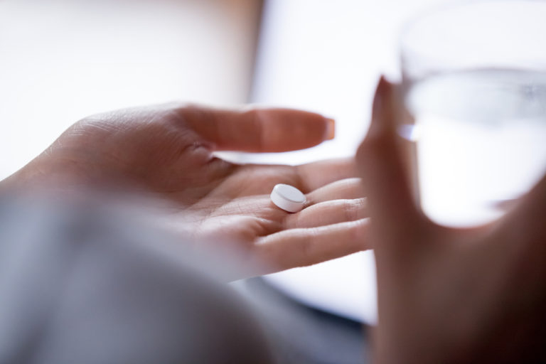woman holding white pill and glass of water